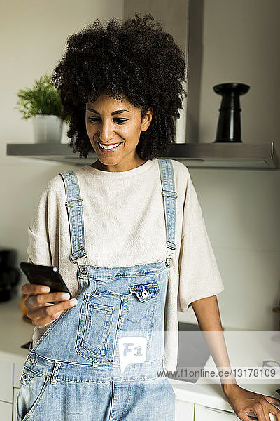 Lächelnde Frau benutzt Mobiltelefon in der Küche zu Hause