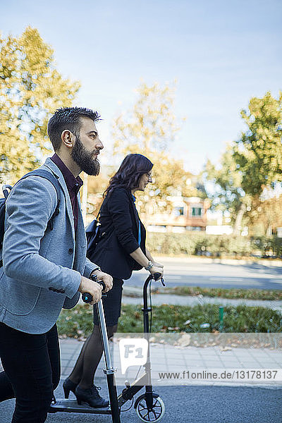 Businessman and businesswoman riding scooter