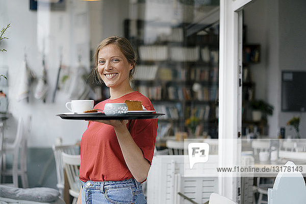 Porträt einer lächelnden jungen Frau  die in einem Cafe Kaffee und Kuchen serviert