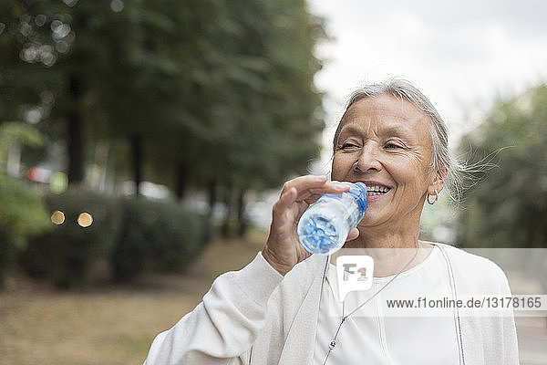 Happy senior woman outdoors drinking water from bottle