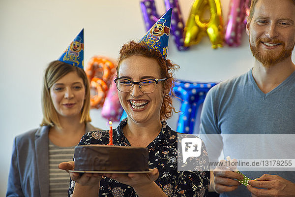Kollegen mit einer Geburtstagsfeier im Büro mit Kuchen und Partyhüten