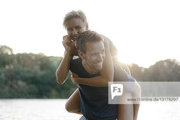 Happy man carrying girlfriend piggyback at a lake