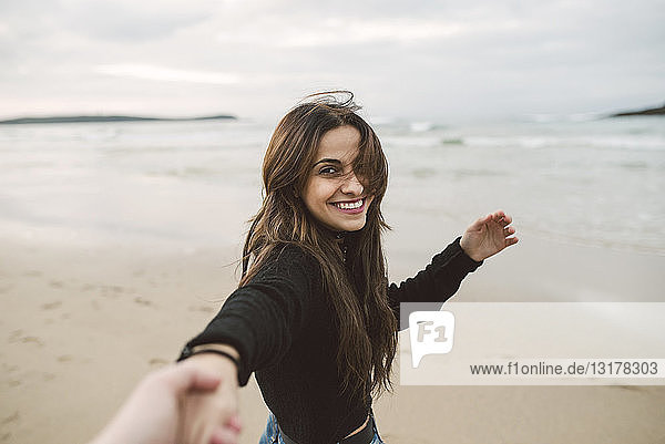 Porträt einer lächelnden jungen Frau  die sich am Strand an den Händen hält
