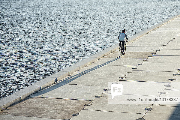 Junger Mann fährt Fahrrad auf der Uferpromenade am Flussufer