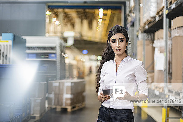 Porträt einer Frau  die eine Tablette in einem Fabriklager hält