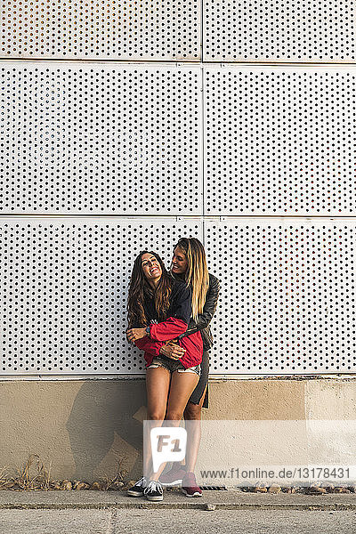 Glückliches lesbisches Paar umarmt sich an einer Wand