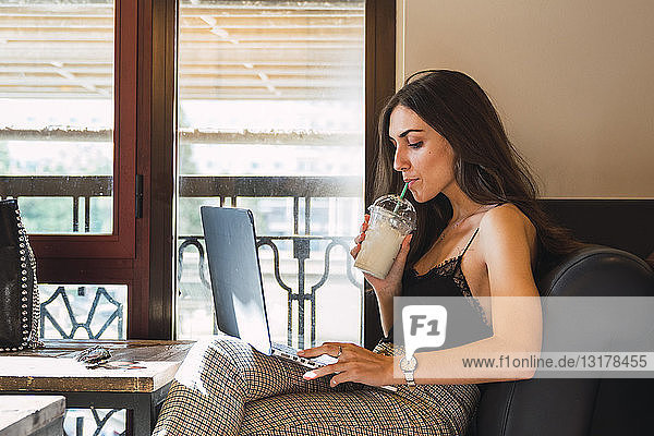 Junge Frau in einem Café  die einen Smoothie trinkt  während sie einen Laptop benutzt
