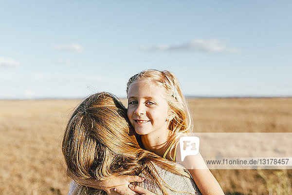 Porträt einer lächelnden Tochter die ihre Mutter auf einem Feld umarmt
