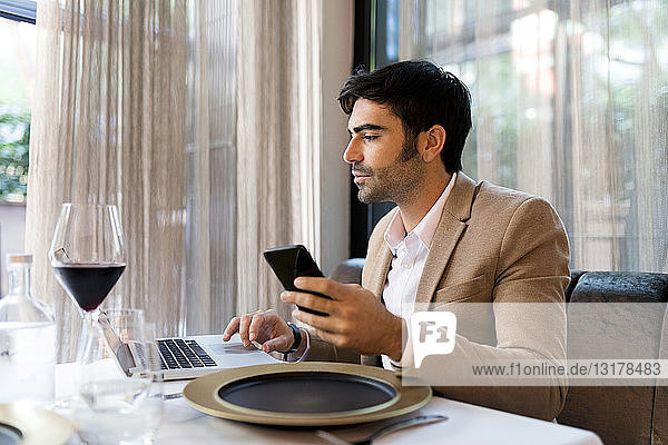 Mann  der in einem Restaurant mit Laptop und Handy am Tisch sitzt