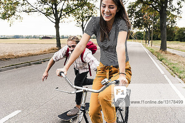 Glückliches junges Paar mit Fahrrad und Skateboard auf der Landstraße