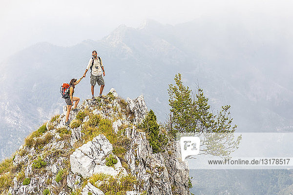 Italy  Massa  man helping woman to climb on top of a peak in the Alpi Apuane mountains