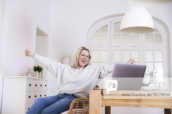 Porträt einer glücklichen blonden reifen Frau mit Laptop zu Hause