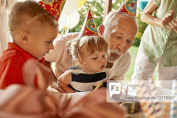 Großvater und Enkel blasen auf einer Gartenparty Kerzen auf dem Geburtstagskuchen aus
