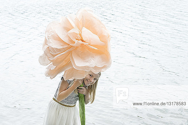 Porträt eines lächelnden blonden Mädchens  das in einem See steht und eine überdimensionale Kunstblume hält