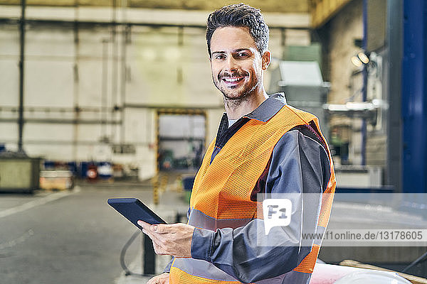 Porträt eines lächelnden Mannes  der eine Tablette in der Fabrik hält