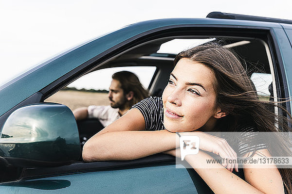 Lächelnde junge Frau lehnt sich aus dem Autofenster