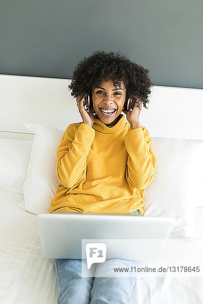 Porträt einer glücklichen Frau  die mit Kopfhörer und Laptop auf dem Bett liegt