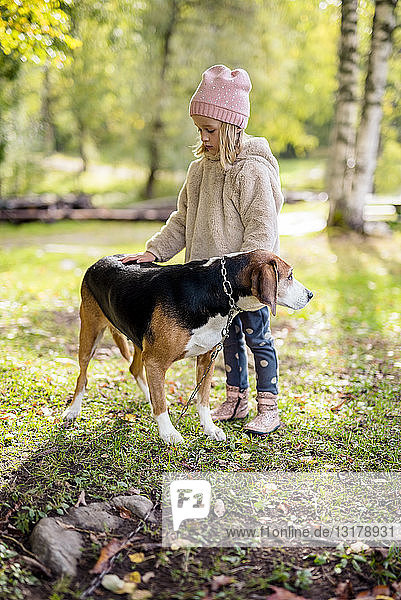 Little girl stroking dog in autumnal garden