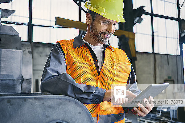 Lächelnder Mann in Arbeitsschutzkleidung mit Tablette in der Fabrik