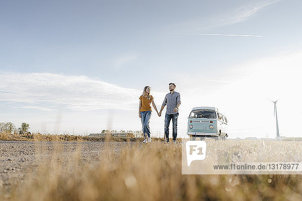 Junges Paar geht auf Feldweg mit Wohnmobil in ländlicher Landschaft