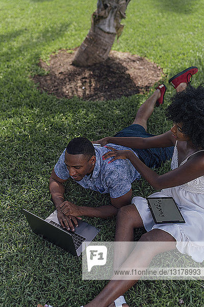 Junges Paar mit Tablett und Laptop auf einem Rasen in einem Park