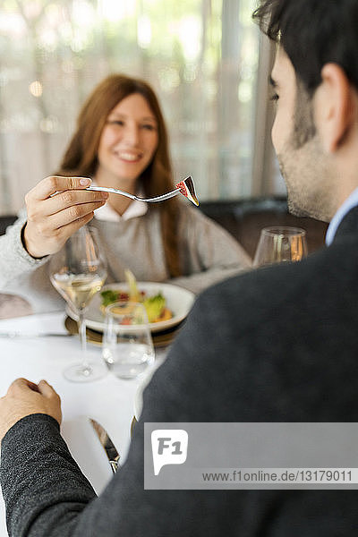 Smiling woman letting man taste the food in a restaurant