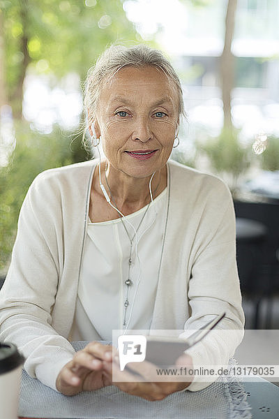 Porträt einer älteren Frau in einem Außencafé mit Mobiltelefon und Kopfhörern