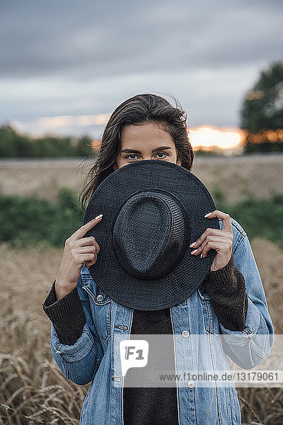 Porträt einer jungen Frau  die sich hinter einem schwarzen Hut versteckt