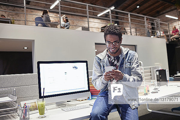 Junger Mann arbeitet in einem kreativen Start-up-Unternehmen und benutzt ein Smartphone