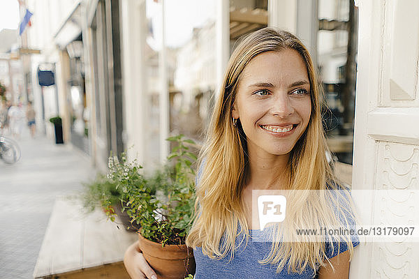 Niederlande  Maastricht  lächelnde blonde junge Frau mit Blumentopf in der Hand in der Stadt