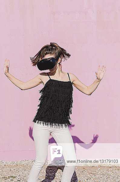 Junge Frau mit VR-Brille bewegt sich vor rosa Wand
