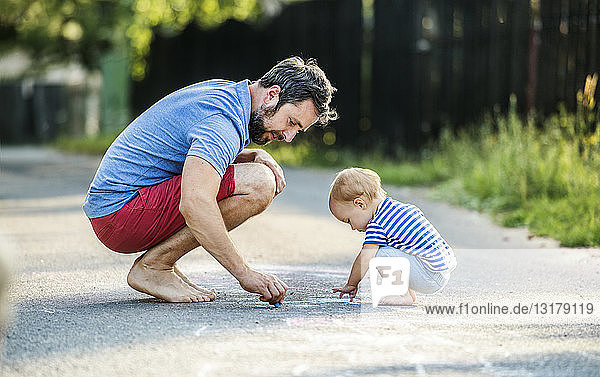 Vater und seine kleine Tochter malen im Sommer mit Kreide auf der Straße