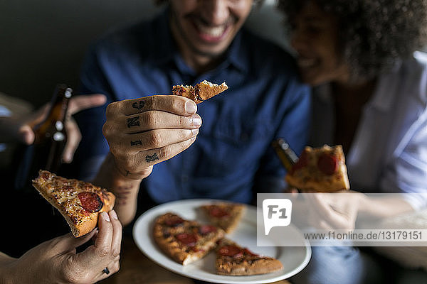 Nahaufnahme eines tätowierten Mannes mit Freunden  die ein Pizzastück in der Hand halten