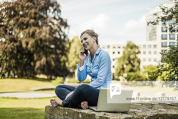 Lächelnde Frau sitzt im Stadtpark und telefoniert