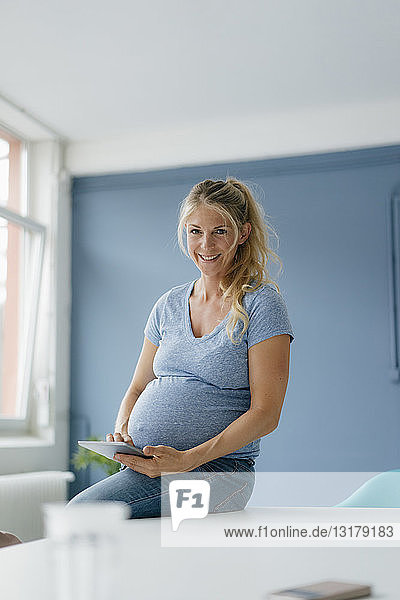 Porträt einer lächelnden schwangeren Frau mit Tablette in der Hand