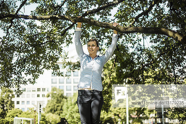 Frau im Stadtpark am Ast eines Baumes hängend