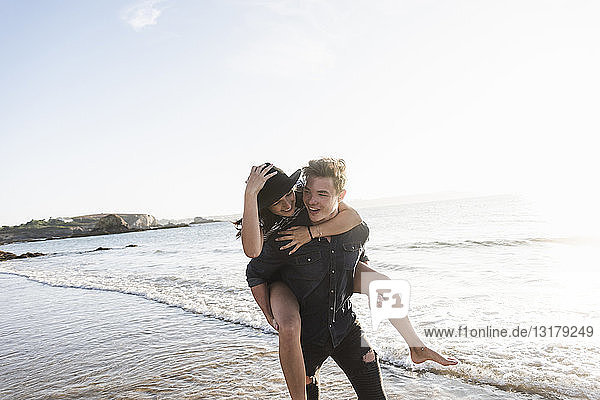 Frankreich  Bretagne  glücklicher junger Mann trägt seine Freundin huckepack am Strand