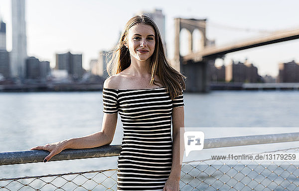 USA  New York  Brooklyn  portrait of smiling woman wearing striped dress standing in front of East River