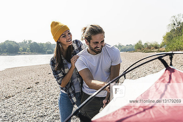 Glückliches junges Paar baut ein Zelt am Flussufer auf