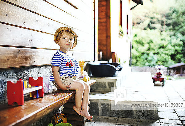 Porträt eines Kleinkindes  das auf einer Bank vor dem Haus sitzt