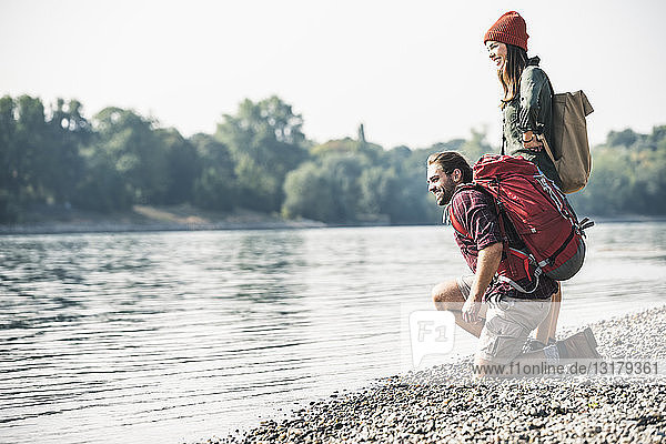 Lächelndes junges Paar mit Rucksäcken am Flussufer