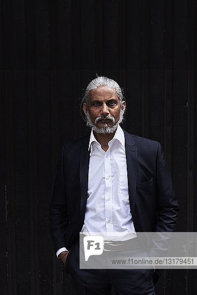 Portrait of stylish senior businessman with grey hair and beard standing against dark background