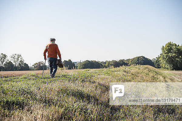 Älterer Mann mit Reisetasche  zu Fuß auf den Feldern