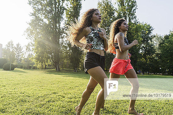 Zwillingsschwestern joggen gemeinsam in der Abenddämmerung in einem Park