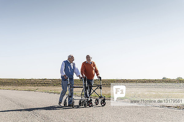 Two old friends walking on a country road  using wheeled walkers