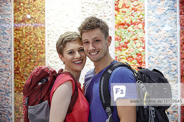 Porträt eines glücklichen Paares mit Rucksäcken an mehrfarbiger Wand