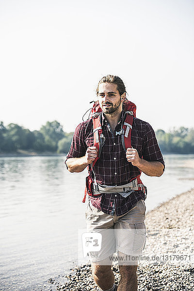 Junger Mann mit Rucksack beim Spaziergang am Flussufer