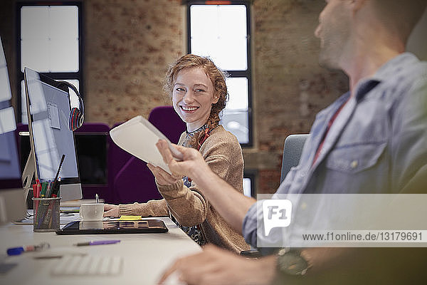 Young man helping colleague sitting at desk in office  smiling
