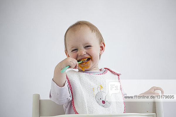 Portrait of laughing baby girl on high chair eating mush