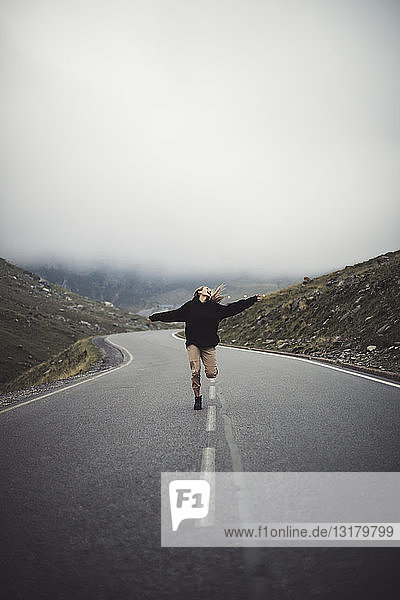 Blonde Frau rennt auf einer Straße mit Bergen im Hintergrund